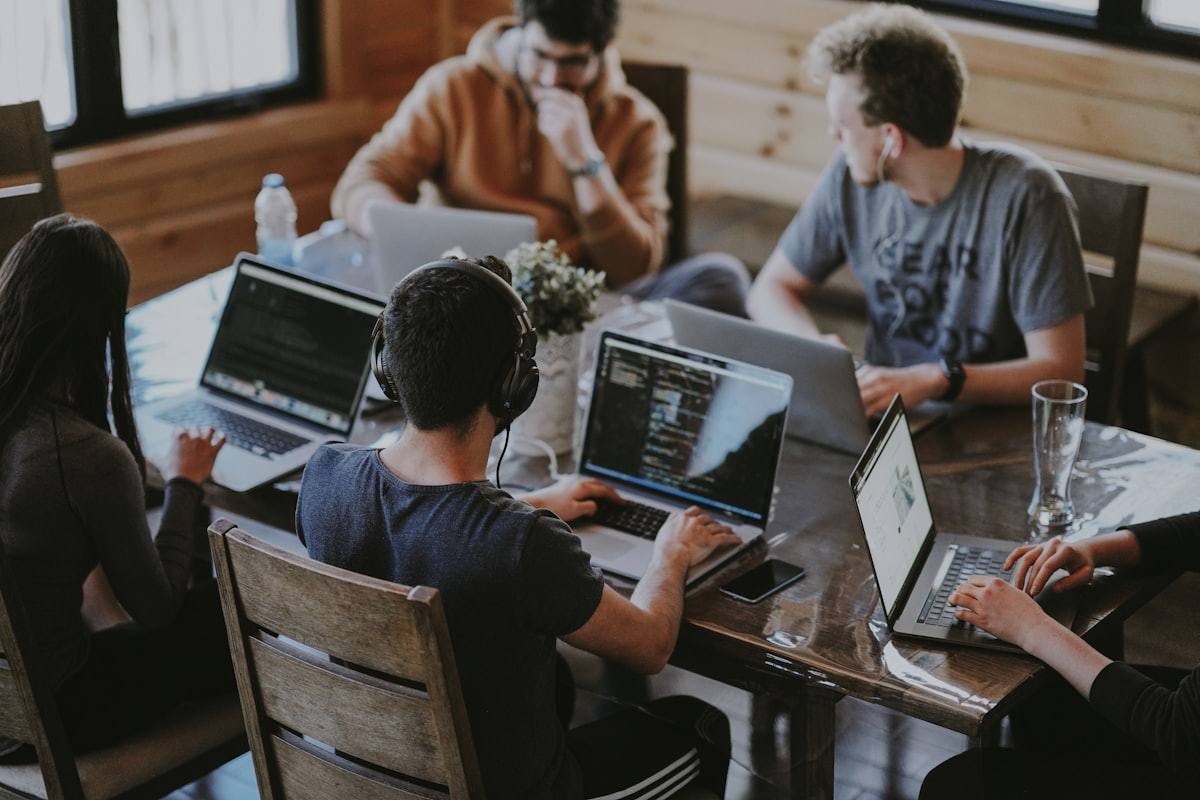 Tim bekerja sama di sekitar meja kayu dengan laptop